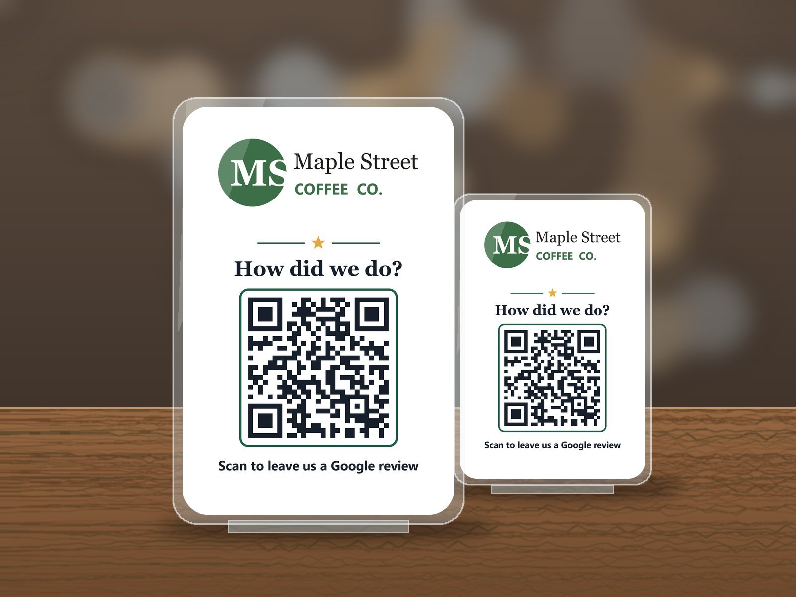 Two clear acrylic stands on a wooden counter, each printed with a coffee shop logo, the words How did we do, and a QR code